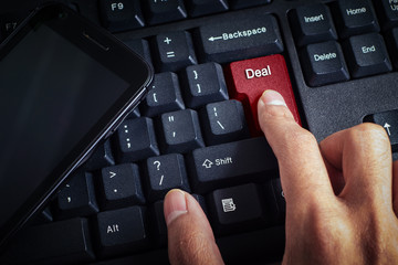 business concept shows the smartphone as well as the fingers that press DEAL on the keyboard