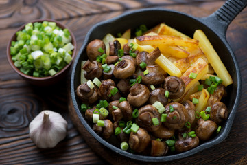 Fried champignons with potato and green onion in a frying pan