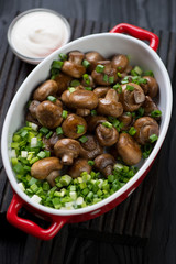 Bowl with whole fried champignons, green onion and sour cream