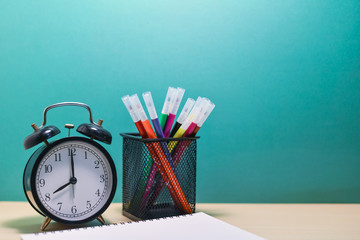 Group of colorful pen,alarm clock and note book on wood table.