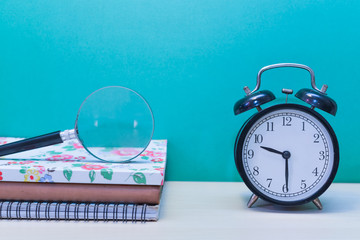 Books,magnifier glass and clock on wooden table with copy space.Green background.