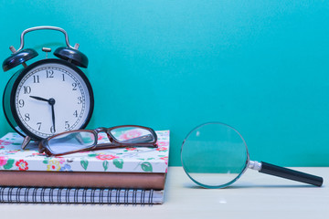 Alarm clock,Books,glasses and magnifier glass on wooden table with copy space.Green background.