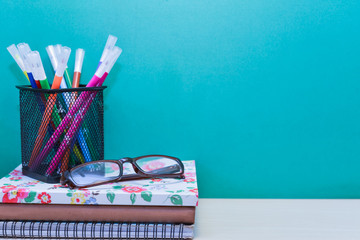 Books,color pens and glasses on wooden table with copy space.Green background.