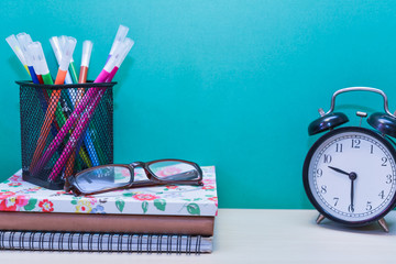 alarm clock,color pens,glasses and Books on wooden table with copy space.Green background.
