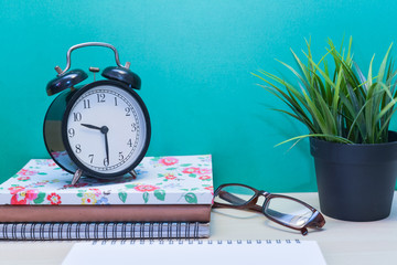 Green Plant,Books,glasses and alarm clock on wooden table with copy space.Green background.