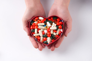 Hands holding different colored medicine and types of pills in heart shaped box on white background