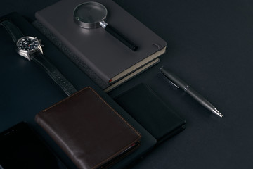 Close up of gentleman set. Magnifying glass, mobile phone, notebook, pen, watch, purse on dark background. Copy space