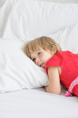 Little girl lies in red dress on white bed