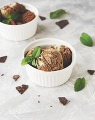 chocolate mint ice cream in white bowls with pieces of chocolate and mint leaves on a marble table