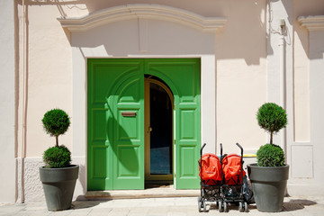 Green door, two plants and red stroller