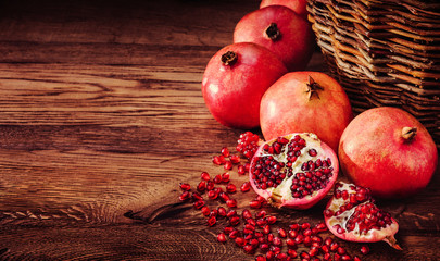 Pomegranate fruit and seeds on wooden background with wicker basket 