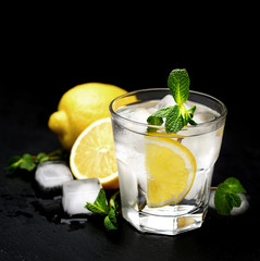 Summer cocktail with soda water, ice, lime and mint on black wooden table. Selective focus