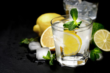 Summer cocktail with soda water, ice, lime and mint on black wooden table. Selective focus