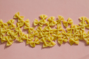 Maсaroni or pasta bow shape in row on pink background