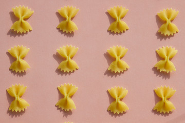 Maсaroni or pasta bow shape in row on pink background