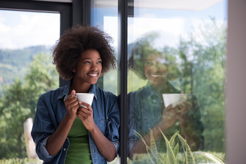 African American woman drinking coffee looking out the window - Powered by Adobe