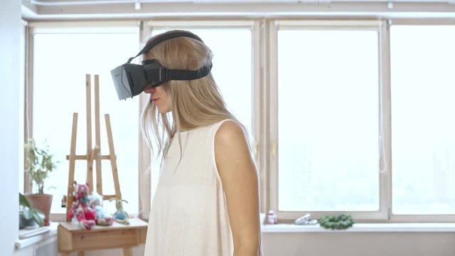 Slow motion of blonde woman in white space trying virtual reality glasses.