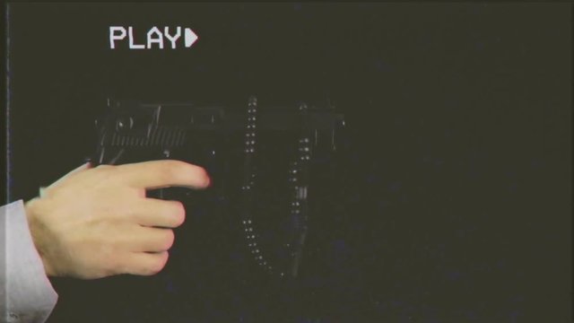 VHS retro fake shot: a hand holding a gun appearing on a black background. A rosary hangs from the barrel of the weapon. Weapon control, murder, danger, faith, religion.
