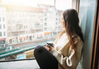 Obraz premium Młoda kobieta chill out przez okno z filiżanką kawy