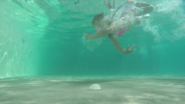 Little girl dives into a pool at the bottom to the shells
