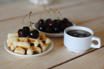 Waffles, cherry and coffee on the wooden table