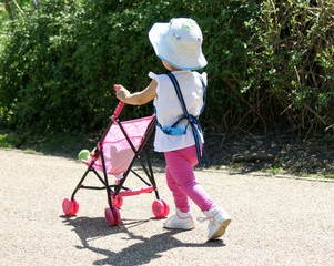 Pretty in pink in the park, toddler taking dolly for a walk in pushchair