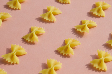 Maсaroni or pasta bow shape in row on pink background