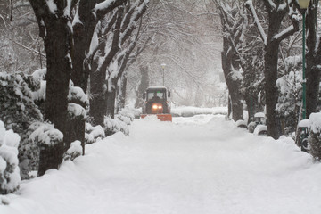 orange tractor driving down snow in a park alley