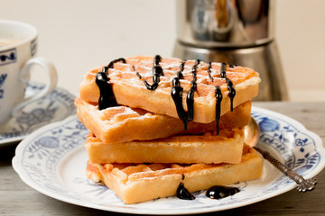 Belgian waffles with chocolate syrup on porcelain plate with blue decor.