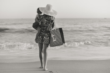 Black and white back side view of mother carrying child walking on sandy beach sunset outdoors background.