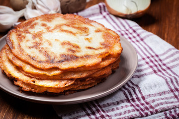 Stack of potato pancakes on a wooden table. In the background po