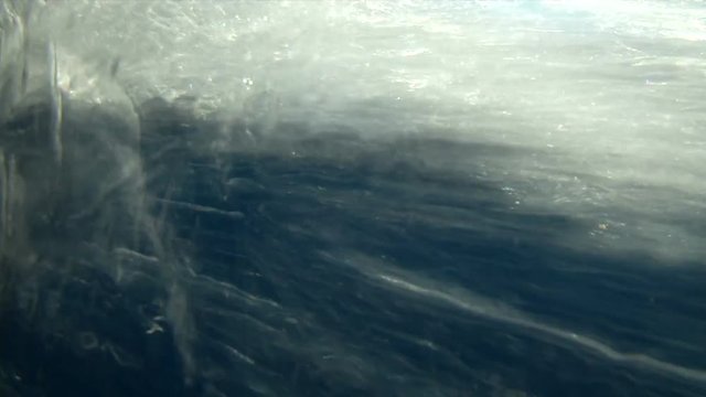 Sea water surface with blue sky and big curly wave splitted by waterline to underwater part with air bubbles (slow motion)