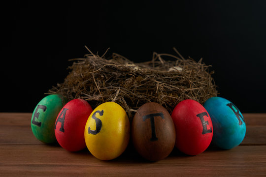 Easter, holidays, tradition and object concept - close up of colored easter eggs and quaill eggs in nest on wooden surface.black background