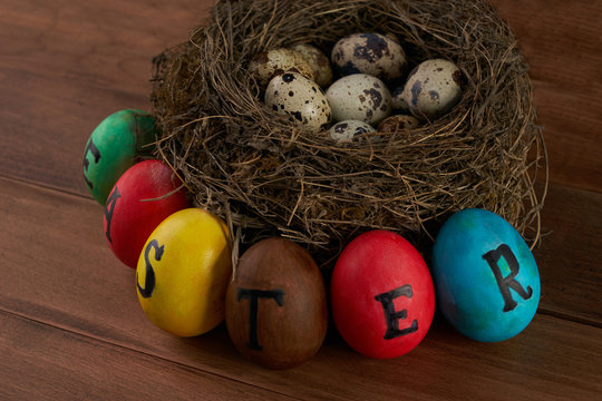 Easter, holidays, tradition and object concept - close up of colored easter eggs and quaill eggs in nest on wooden surface