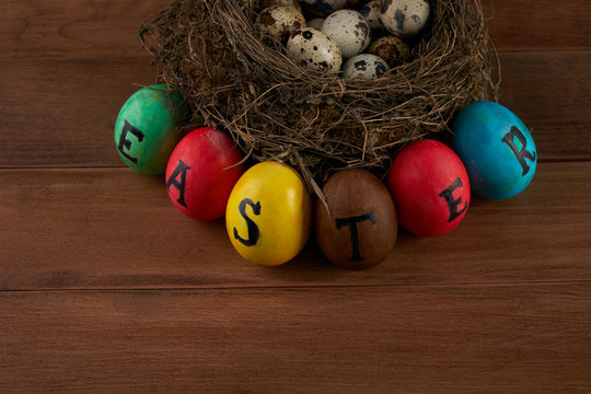 Easter, holidays, tradition and object concept - close up of colored easter eggs and quaill eggs in nest on wooden surface.Top view.