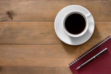 Hot cup of Americano coffee morning breakfast with red notebook and pen on classic old vintage brown wooden top view background.