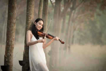Young beautiful woman playing violin in the forest.