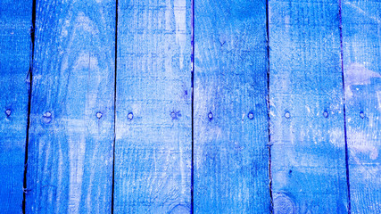 Fototapeta na wymiar Blue vetical wooden planks with screws on the middle of every plank with cracked paint and some white spots. texture of old wooden planks with cracked and smeared paint
