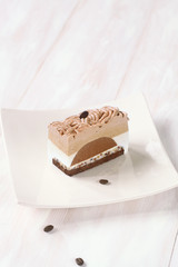 Piece of Contemporary Chestnut and Coffee Mousse Cake, on white plate, on wooden background.