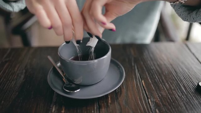 Woman closeup strewing sugar to cup of coffee in a cafe