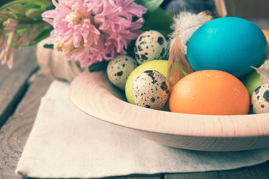 Easter colorful and quail eggs in wooden pot with pink hyacinth on dark wooden table. Toned photo.
