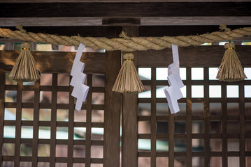 Close-up detail of shimenawa rope and paper streamers known as shide in front of a wooden grid door at a Japanese Shinto shrine. Travel and religion concept.