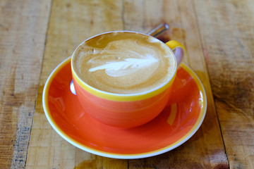 Top view of cappuccino coffee with art dress up in orange cup on