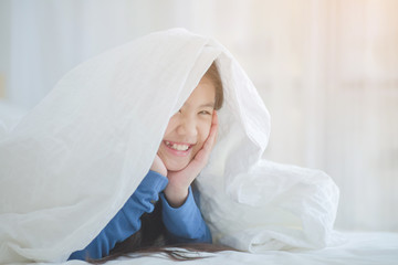 Happy smiling Asian girl playing hide and seek under the blanket in her bed room