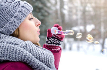 Young beautiful woman blowing bubbles  in winter clothing outdoors.  Focus on lips. Soup bubbles.