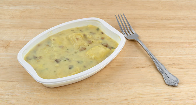 Ravioli in a cheese and mushroom sauce TV dinner atop a wood table with a fork to the side.