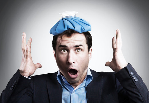 Shocked Office Worker With An Ice Pack On His Head. Unpaid Sick Leave Concept