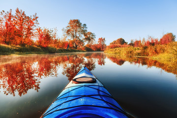Blue kayak sailing down a river on a sunny autumn day against yellow foliage trees and fog reflected in the water. Exploration of wild pristine nature and wanderlust concept.