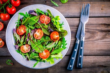 Fresh salad with mixed greens and cherry tomato on wooden background