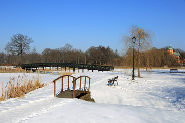 Piękny park zimą, most, latarnie i ławeczki.
